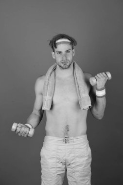 Çıplak gövdeli bir adam havluyu boynunda ve dambıllarında tutuyor.