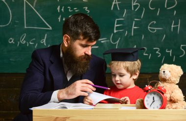 Öğretmen, evde tek tek çocuk çalışmaları. Öğretmen ve öğrenci kolej, kara tahta arka plan içinde. Sakal, oğlum, küçük çocuk öğretmen öğretir Peder. Bireysel eğitim kavramı