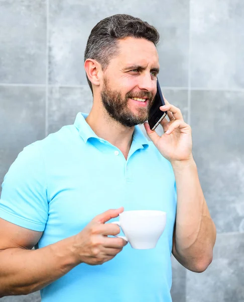 Hombre beber cappuccino hablar teléfono gris fondo de la pared. El café puede ser interminablemente reimaginado hacer algo nuevo como emprendedores artesanos y reinventar negocios. Descanso agradable café en el trabajo — Foto de Stock