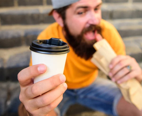 Hipster bite eat hot dog. Fast food meal for lunch. Hipster bite hot dog hold drink paper cup. Man bearded enjoy quick lunch stairs background. Energy from street food daily traditional snack