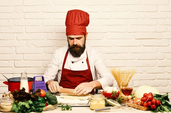 Cook with serious face in burgundy uniform sits by table