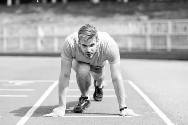 Man runner on start position at stadium. Runner in start pose on running surface. Man run outdoor at running track. Sport and athletics concept. Sportsman on concentrated face ready to go
