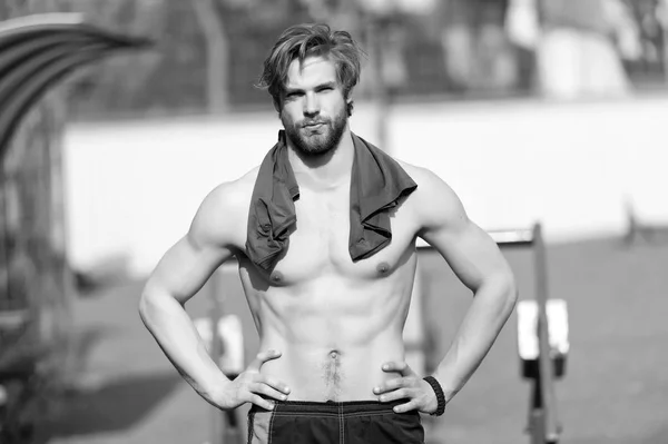 Uomo barbuto con muscoli del busto in forma allo stadio. Sportivo con maglietta blu sul collo. Atleta con ventre e petto sexy all'aperto soleggiato. Allenamento e allenamento. Sport o fitness e cura del corpo — Foto Stock