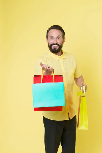 Offrir un bonus pour le client bonne idée. Homme mature barbu visage joyeux tient des sacs à provisions. L'homme a des dons inattendus. Guy surpris par le cadeau fond jaune. Les présents rendent nos vies plus intéressantes — Photo