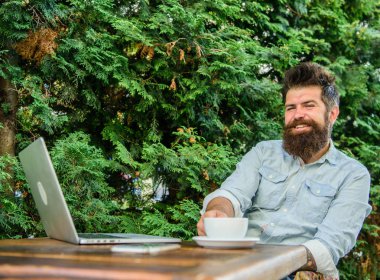 Hoş bir an. Düşünmek için zaman ayırın. Dinlenmek için mola. Sakallı adam hipster yapmak için kahve içmek duraklatmak ve dizüstü bilgisayar ile oturup süre düşünüyorum. Adam kahve rahatlatıcı Teras yeşil dallar arka plan içecekler