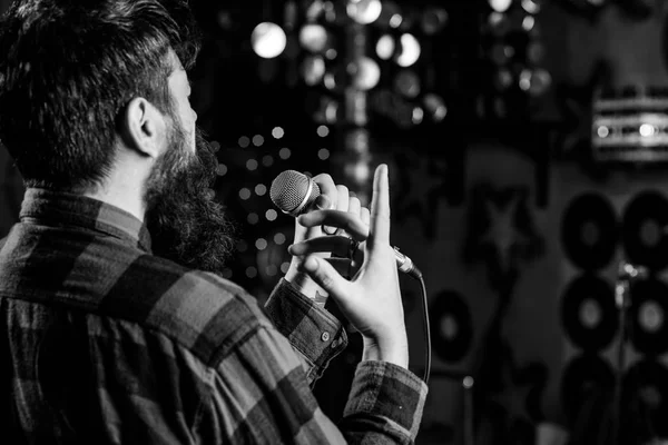 Músico com barba cantando música em karaoke, vista traseira. Conceito de cantor de rock. Homem de camisa quadriculada detém microfone, canto canção, karaoke fundo clube. O tipo gosta de cantar no salão de karaoke escuro. — Fotografia de Stock