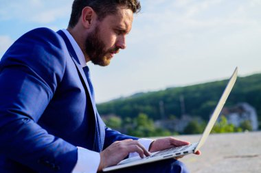 Internet Pazarlama Yöneticisi mavi gökyüzü arka çalışır. Oranları online satış ipuçları artırın. İşadamı sörf internet veya yanıt e-postalar ile dizüstü bilgisayar açık havada oturup süre. Nasıl yüksek yanıt oranları elde