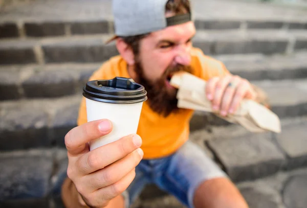 Brodaty mężczyzna pokazuje kubek napój schody tło. Kawę można zabrać ze sobą. Posiłek Fast food na obiad. Hipster bite hot dog trzymać kubek papierowy napój. Energia z ulicy żywności codziennie tradycyjne przekąski — Zdjęcie stockowe