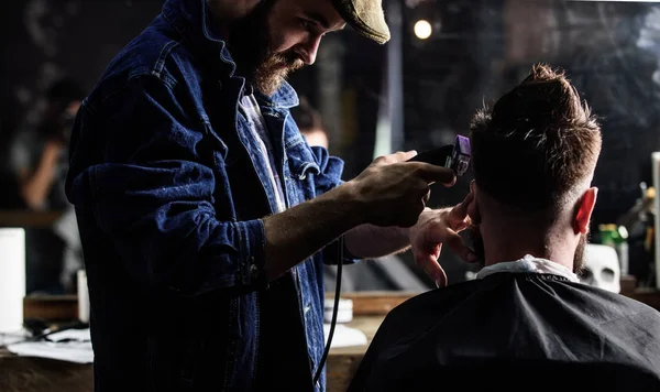 Barber med clipper trimning hår av klienten, bakifrån. Frisör med hårklippare fungerar på frisyr av skäggig kille, barbershop bakgrund. Hipster klienten få frisyr. Hipster livsstilskoncept — Stockfoto