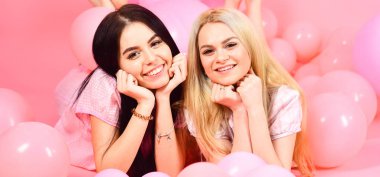 Dedikodu kavramı. Sarışın ve esmer gülümseyen yüzler üzerinde yerli yatak partide iyi eğlenceler. Kız ya da arkadaşlarım pijama kız gibi pijama partisinde. Balonlar, pembe bir arka plan yakınındaki göbek kızlar yatıyordu