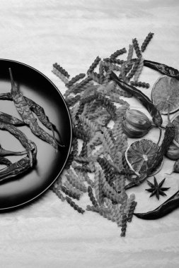 Kırmızı biber ve siyah seramik tabak içinde makarna ve malzemeler.