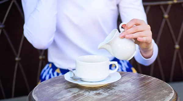 Tips for healthier coffee drinking. Coffee always better with milk. Hand female adding milk to black coffee outdoors cafe terrace, close up. Mug americano or black tea and jug with milk