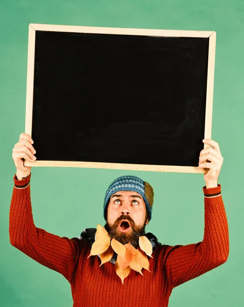 Man in hat looks up at blackboard on green background