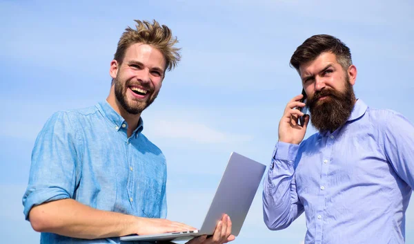 Men with laptop and smartphone solving problems using mobile internet. Workers with gadgets always having access to mobile internet. Always online. Business team works outdoor, sky background