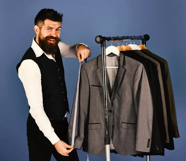 Tailor with happy face holds measuring tape near custom jackets — Stock Photo, Image
