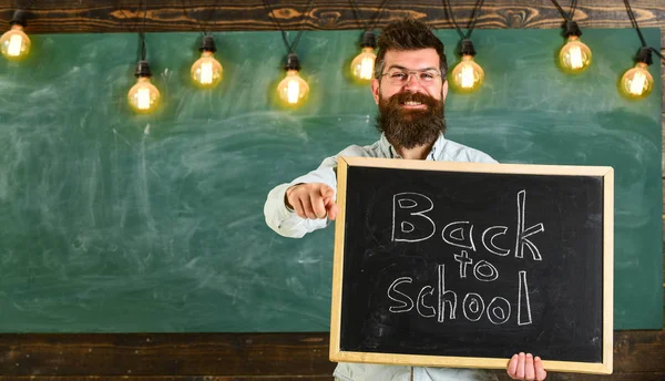 Professeur de lunettes tient tableau noir avec inscription de retour à l'école. Homme avec barbe et moustache sur le visage heureux invite les étudiants, pointant vers l'avant, tableau sur fond. Concept de retour à l'école — Photo