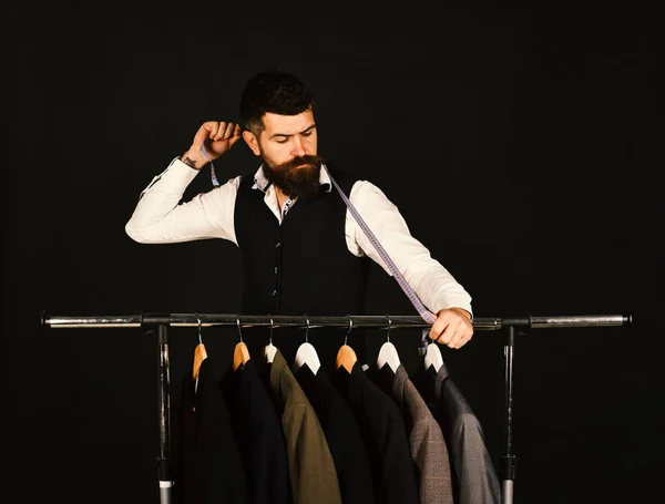 Tailor with serious face holds measuring tape near custom jackets — Stock Photo, Image