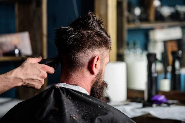 Main de coiffeur avec tondeuse à cheveux gros plan. Hipster barbu client obtenir coiffure. Concept de salon de coiffure. Homme avec barbe dans une chaise de coiffeur, fond de salon. Barbier avec tondeuse à cheveux coupe nuque — Photo