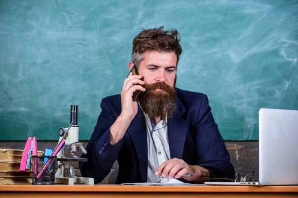 Em contacto com a escola. Diretor da escola ou professor chamando os pais para relatar sobre os resultados do exame. Homem com barba falar telefone sala de aula fundo. Professor da escola se preocupa com a comunicação com os pais — Fotografia de Stock