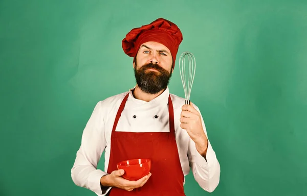 Koken met zelfverzekerde gezicht in uniform houdt kom en klop. — Stockfoto