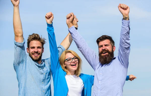 Company of three happy colleagues or partners celebrating success, sky background. Success concept. Men with beard in formal shirts and blonde in eyeglasses as successful team. Company reached top.