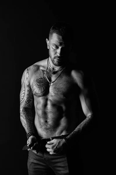 Man with tattoo design on skin. Fashion model buckle leather belt in jeans. Bearded man shirtless with fit torso. Sportsman with six pack and ab. Fitness with sport and bodycare, black and white — Stock Photo, Image