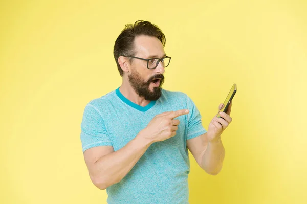 Guy eyeglasses cheerful pointing at smartphone. Man happy user interact application for smartphone. Man takes advantages online communication. Guy bearded interact mobile interface application