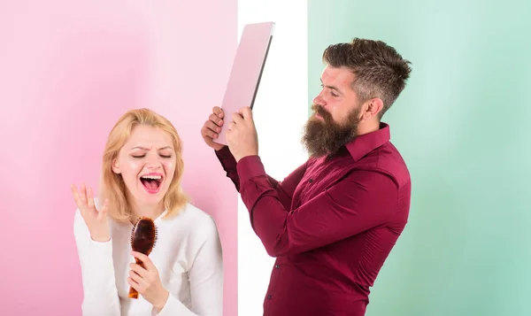 Lady sing using hair brush as microphone while man annoyed going beat her laptop. Better sing at talent show than at work. Lady imagine she superstar talented singer. Can not stop song in her head