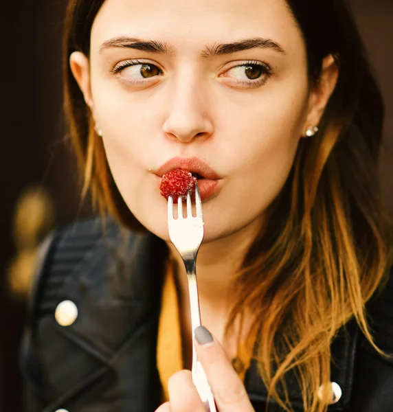 Lady holds dessert fork with raspberry near mouth