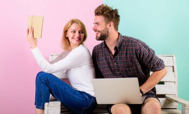 Couple spend leisure with book and movie. Book evokes real human emotions. Girl interested enthusiastic reading book near guy with modern laptop watching film. Book better than movie clipart
