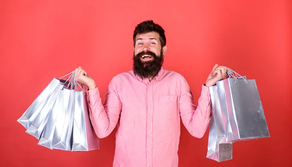 Typen, die in der Verkaufssaison mit Rabatten einkaufen. Mann mit Bart und Schnurrbart hält Einkaufstaschen, roter Hintergrund. Verkauf und Rabattkonzept. Hipster mit glücklichem Gesicht ist einkaufsüchtig oder shopaholic — Stockfoto
