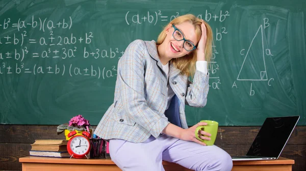 Tómese un descanso para relajarse. Condiciones de trabajo para los profesores. Condiciones de trabajo que deben tener en cuenta los futuros profesores. Mujer sonriente profesor sostiene taza beber sentarse mesa aula pizarra fondo — Foto de Stock