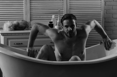 Güçlü kolları olan, küvette çıplak oturan maço. 