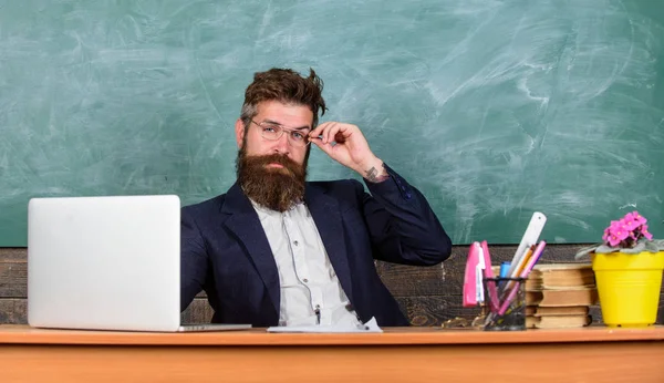 Я твой новый учитель. Учитель бородатый хипстер в очках сидит на фоне школьной доски. Учитель сидит за столом с ноутбуком. Вернемся к школьной концепции. Школьный учитель готов начать урок — стоковое фото