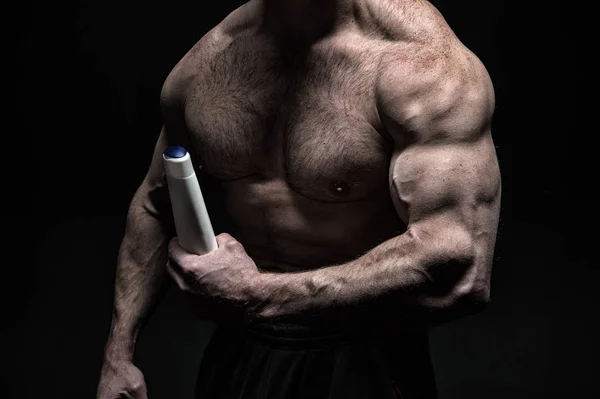 Hand muskulösen Bodybuilder hält Plastikflasche. Hautpflegemittel. muskulöser Brustsportler auf schwarzem Backboden. Produkt für Körperpflege und Hautpflege. Körperlotion männlich. Lotion hygienische Kosmetik — Stockfoto