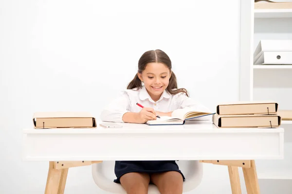 Άριστος μαθητής. Κορίτσι παιδί γράφει hometask ενώ κάθονται τραπέζι λευκό φόντο. Μαθήτρια μελετώντας γραπτώς δοκίμιο. Παιδί κορίτσι σχολείο στολή χαρούμενο πρόσωπο ασκεί hometask, αντιγράψτε χώρο — Φωτογραφία Αρχείου