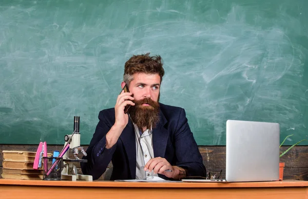 Tartsuk a kapcsolatot. Iskolai tanár hívás mobil telefon, miközben ül tanterem Palatábla háttér. Tanár szakállas férfi beszélgetés mozgatható telefon. Hívás kolléga tanácsot kérni. Pedagógus tarthatja a kapcsolatot munkatársaival — Stock Fotó