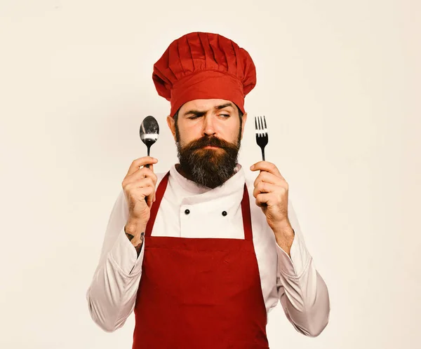 Hombre con barba sostiene tenedor y cuchara sobre fondo blanco. — Foto de Stock