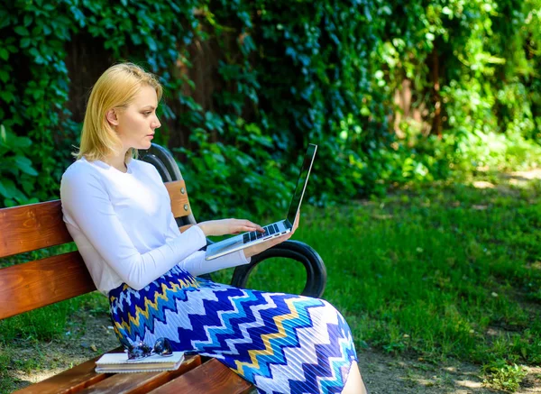 Surfing net in nature. Woman with laptop works outdoor, green nature background. Lady freelancer internet surfing or working in park. Girl sit bench with notebook. Free time surfing internet in park