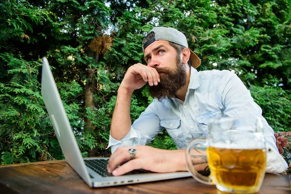 Betting and real money gaming. Brutal man leisure with beer and sport game. Football fan bearded hipster make bet sport game laptop. Guy sit terrace outdoors with beer. Bet on world championship