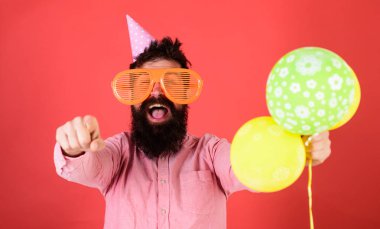 Hippi dev güneş gözlüğü Doğum günü kutluyor. Sakal ve bıyık mutlu yüz tutan grup hava balonları, kırmızı arka plan üzerinde olan adam. Doğum günü partisi konsepti. İleriye dönük parti şapkalı adamı.