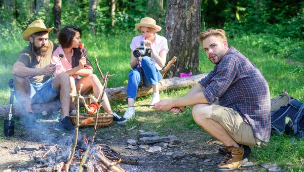 Hike picnic ideas. Hikers sit near campfire relaxing while wait roasting food. Hikers organized quick picnic to eat and relax. Hikers spend leisure in forest nature background. Youth hiking vacation