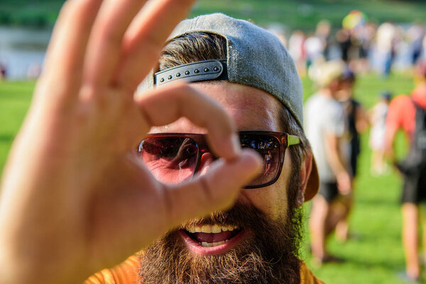 Мужчина бородатый на фоне толпы на берегу реки. Будьте уверены на летних каникулах. Забронируйте билеты на летний фестиваль заранее. Фестиваль посещений хипстеров. Мужчина веселое лицо смотрит сквозь хорошо жест
