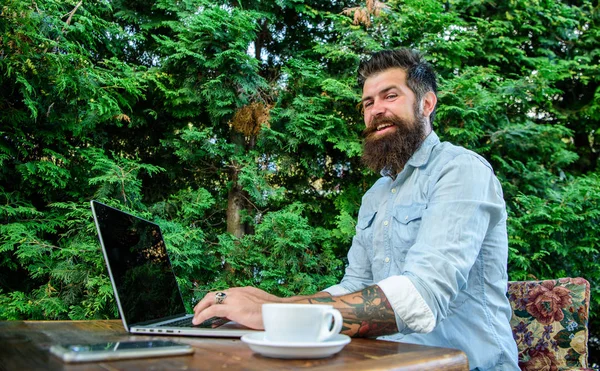 Hipster freelancer work online blog notebook. Blogger create post while enjoy coffee. Man bearded businessman sit terrace with laptop and cup of coffee. Freelance benefit. Create content for web blog