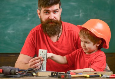 Küçük Yardımcısı kavramı. Evlat, Çocuk koruyucu kask meşgul el ile baba ile onarım yapar. Baba sakallı sınıfta, arka plan kara tahta araçlarını kullanmak için küçük oğlu öğretim