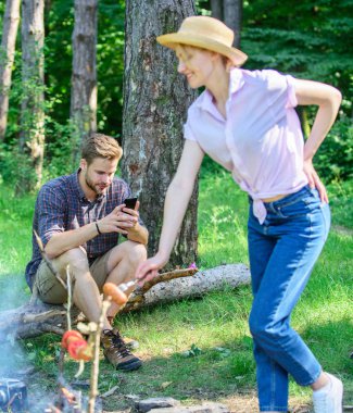 Adam kız gıda ateşte kavurma sırasında smartphone ile meşgul. Aile pikniği doğa arka plan. Aile piknik rahatlatıcı yürüyüş veya tatil hafta sonu. Tatil bile o arkadaşları temas kalmak