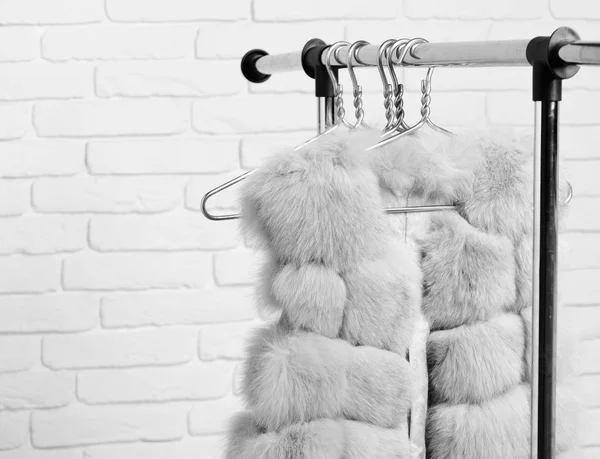 Μοντέρνο πολυτελές παλτό μέση της γούνας κρέμεται σε rack σε χρυσό κρεμάστρες σε φόντο στούντιο τοίχο τούβλο. — Φωτογραφία Αρχείου