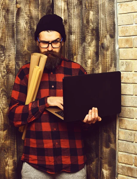 Bearded brutal caucasian hipster holding laptop and craft paper — Stock Photo, Image