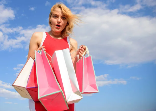 Frau rotes Kleid trägt Bündel Einkaufstüten blauen Himmel Hintergrund. Mädchen mit Einkäufen zufrieden. Einkaufen ist der beste Weg, um die Stimmung zu steigern. Verkauf und Rabatt machen sie glücklich. endlich Lieblingsmarken gekauft — Stockfoto
