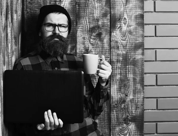 Skäggig brutal kaukasisk hipster som håller laptop med kopp — Stockfoto